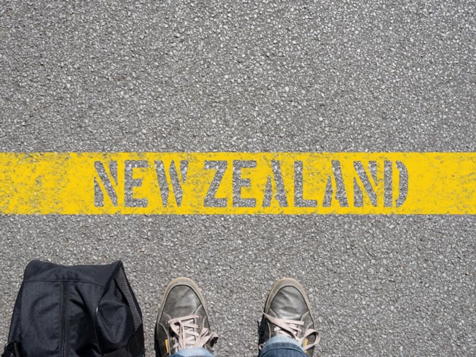 Auswandern nach Neuseeland, Vogelperspektive auf zwei Füße und eine Tasche vor einer Bodenmarkierung „New Zealand“, Foto: stadtratte/stock.adobe.com