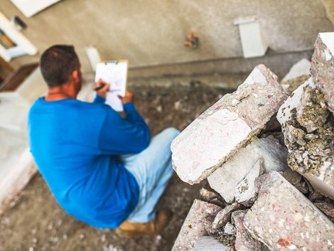 Ein Sachverständiger hockt vor einer Gebäudewand die er inspiziert, Foto: iStock.com/Cat Lane