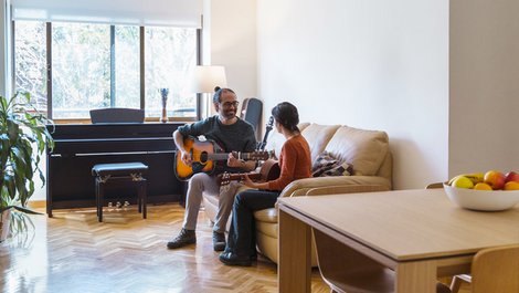 Homeoffice steuerlich absetzen, Gitarrenlehrer mit Schülerin auf dem Sofa bei Gitarrenunterricht, Foto: beavera / stock.adobe.com