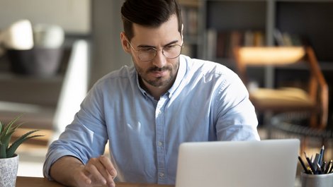 Instandhaltungsrücklage, ein Foto von einem Mann mit Brille, der vor einem Laptop sitzt und auf einen Taschenrechner tippt, Foto: fizkes / stock.adobe.com