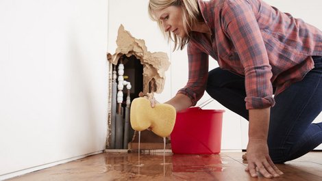 Eine Frau nimmt mit einem Schwamm Wasser vom Boden auf. Foto: Monkey-Business / stock.adobe.com