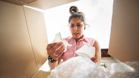 Transportversicherung, Junge Frau schaut in den Karton und hält Scherben in der Hand, Foto: iStock.com / ArtistGNDphotography